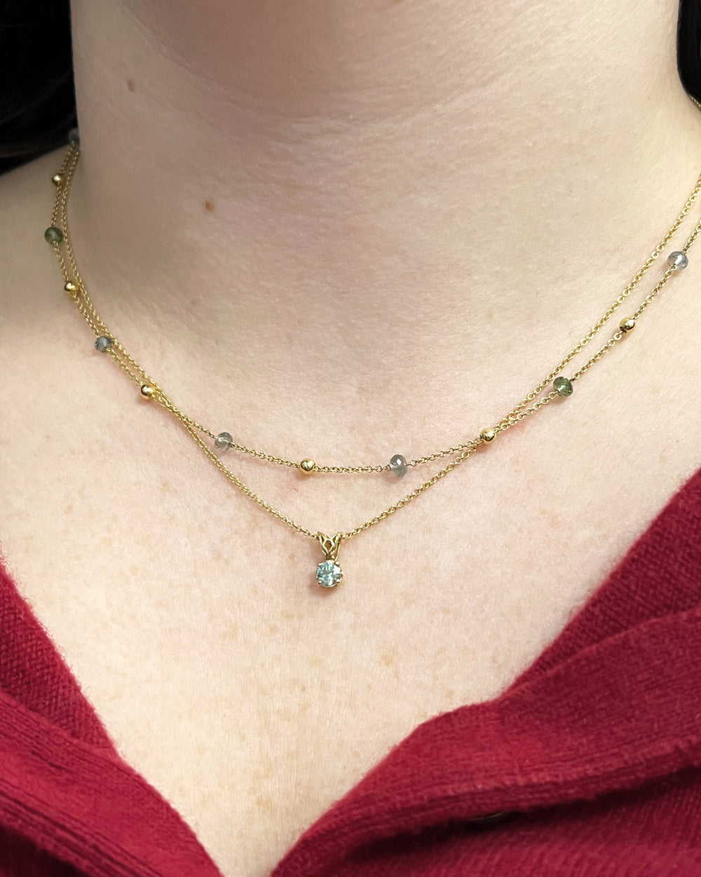 Close-up view of a woman's neck donning the Montana sapphire pendant in 14k yellow gold with a light blue-green 0.49ctw sapphire and high polish finish. Designed and made in the Seattle studio of Green Lake Jewelry Works. Explore more Montana sapphire jewelry online.