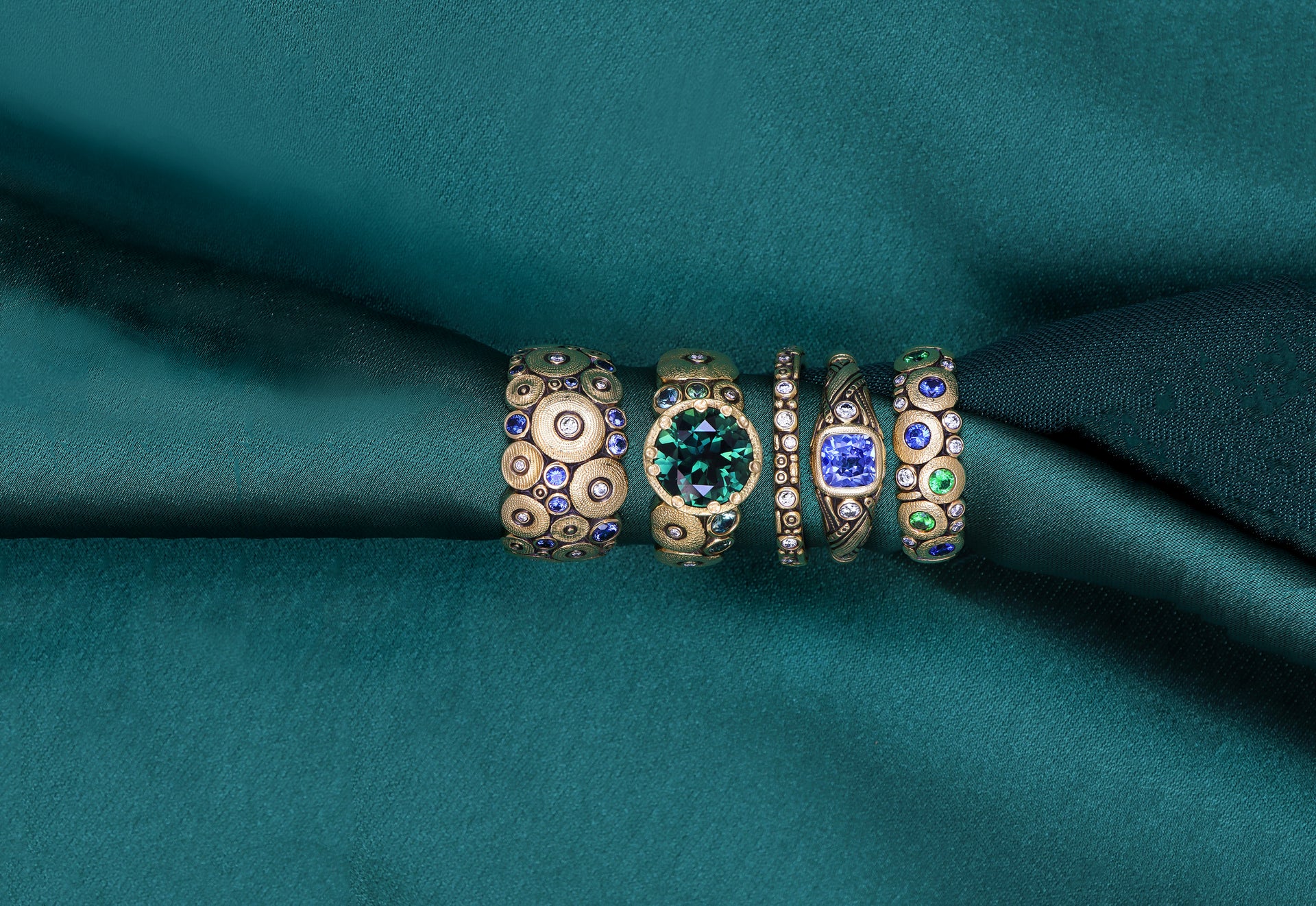 Alex Sepkus gold rings with green and blue sapphires on green fabric