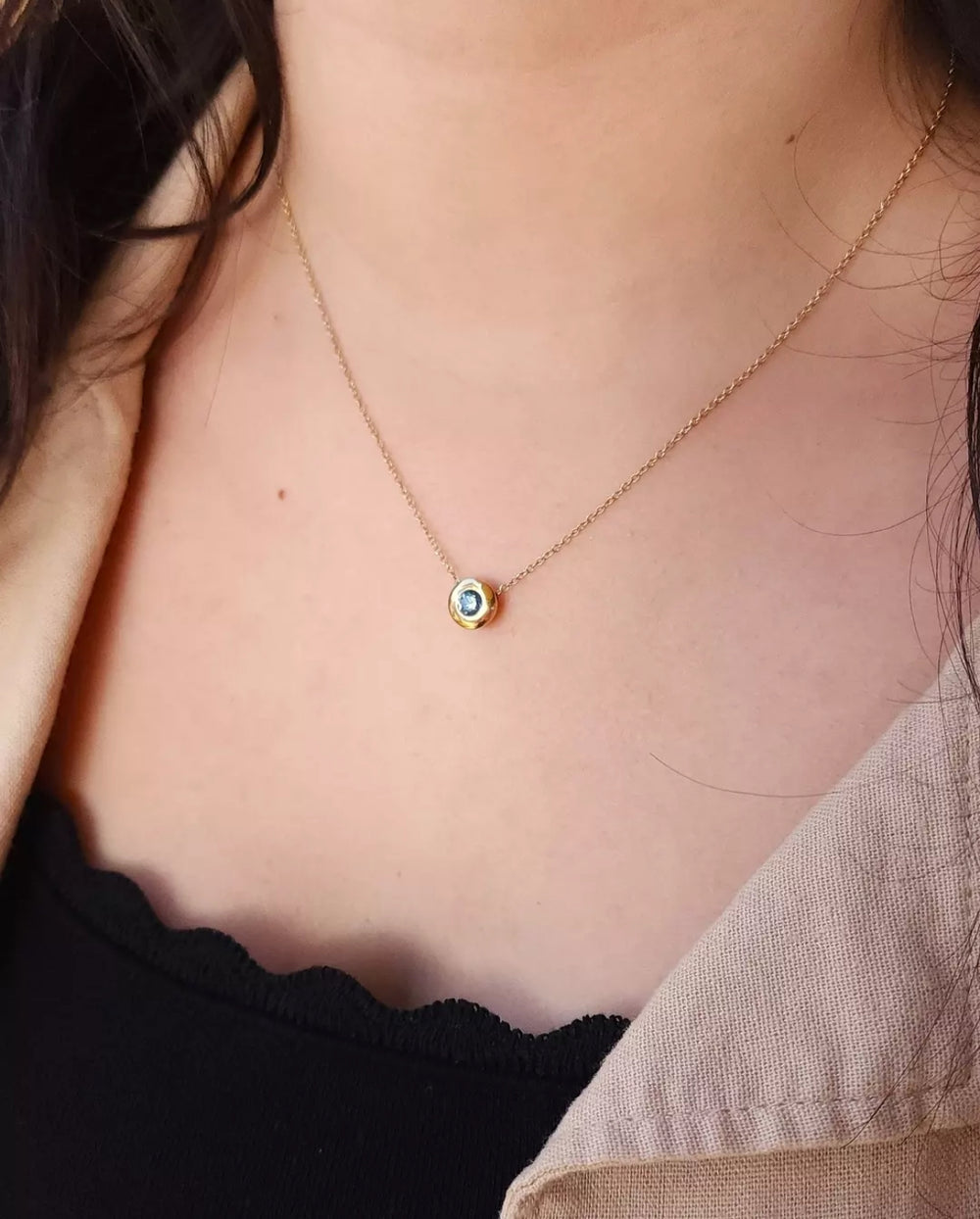 Close-up view of a woman's neck donning the Montana sapphire pendant with a 0.68ctw round sapphire in a 14kt yellow gold puffy bezel slide setting on an adjustable cable chain. Designed and made in the Bellevue studio of Green Lake Jewelry Works. Explore more Montana sapphire jewelry online.