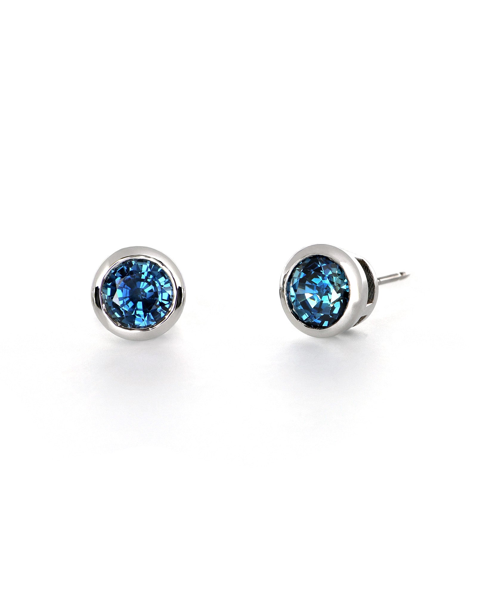 vivid blue sapphire set in bezel stud earrings. laid out on a white background