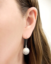 Close up of lady's ear wearing silver earrings  with long hook and a round enamel element