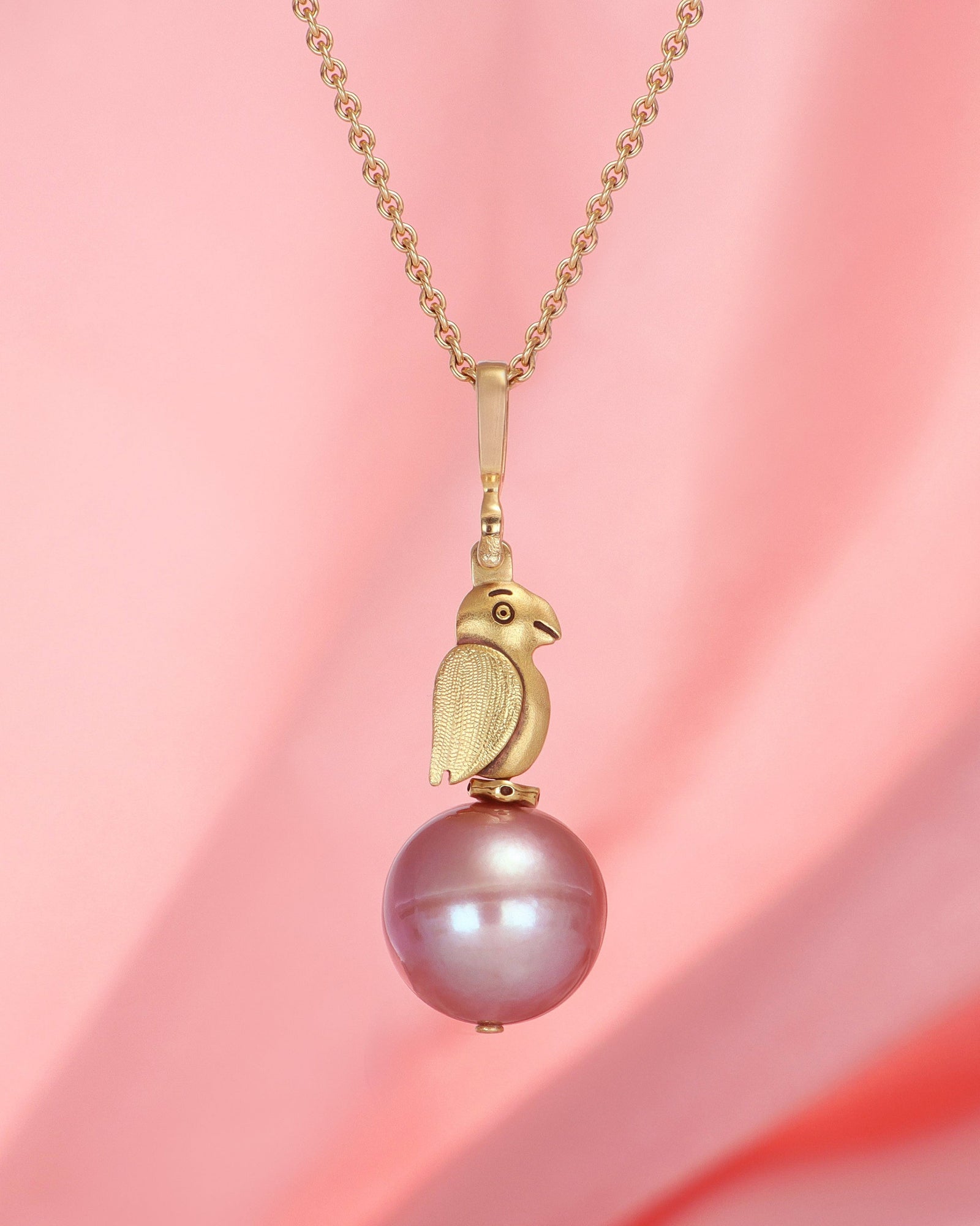 Gold necklace with a pink pearl pendant on a pink background
