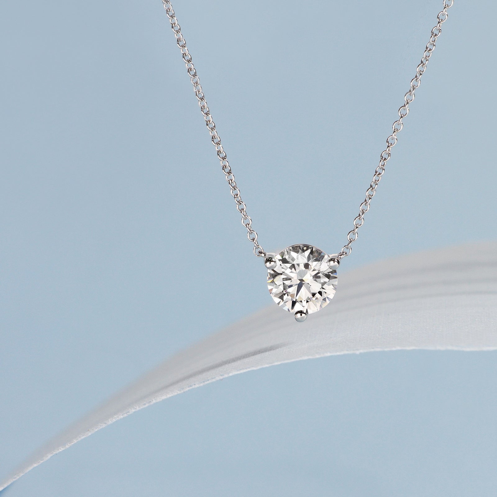 Round diamond solitaire pendant on a chain against a light blue background