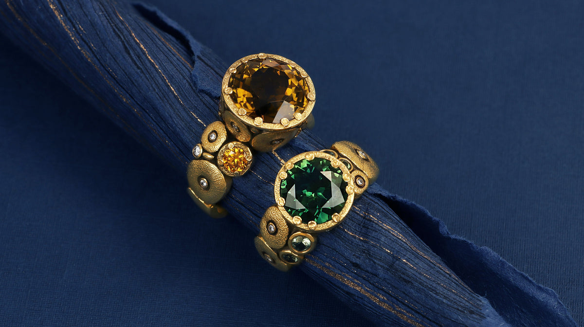 two  strimg gold rings made by alex sepkus, both with iconic texture gold, one with a rich yellow stone, one with a vibrant green stone